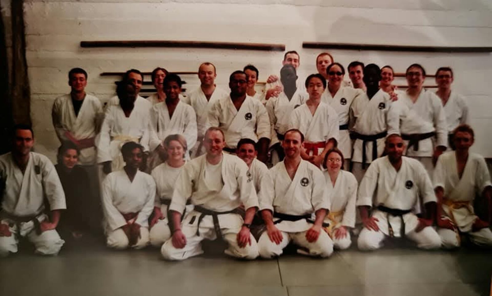 Archive photograph of a full DKK class in the dojo, bo staffs racked on the wall behind