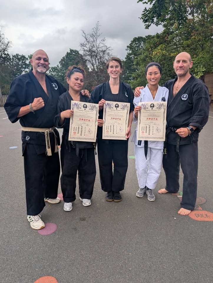 Marianette Violeta, Catherine Sandwell and Mizuki Murai holding their Sandan certificates outdoors, flanked by two senior grades